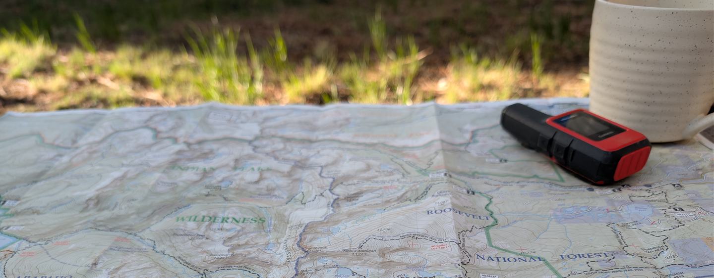 A map, GPS, and coffee mug laid out for review in the sun