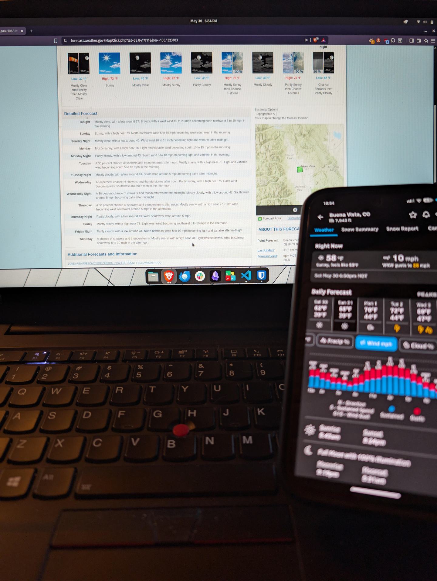 A laptop with a phone both showing upcoming weather forecasts — studying the variables.