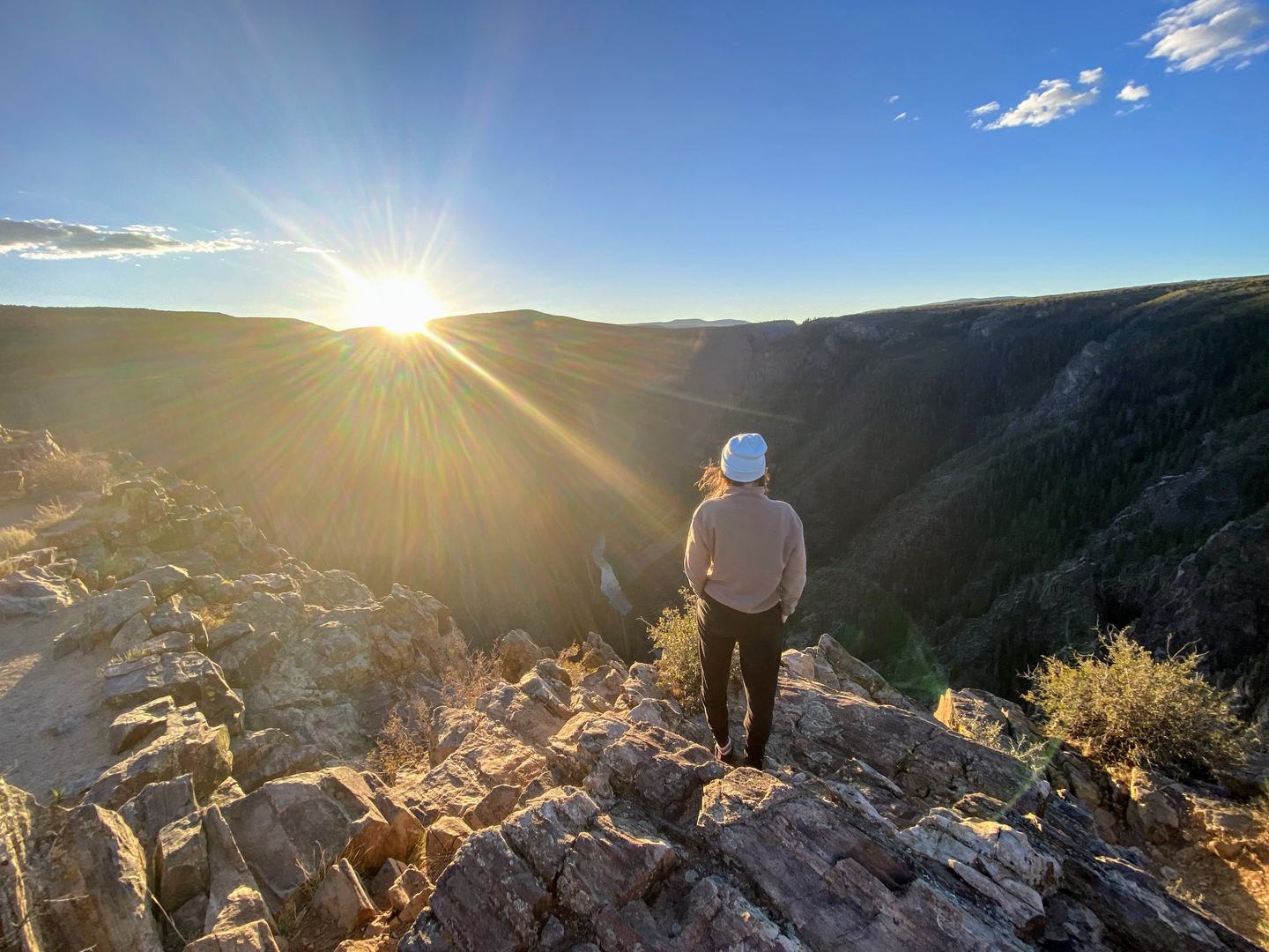 A person standing on a rock outcropping looking at the sun rising in the backcountry
