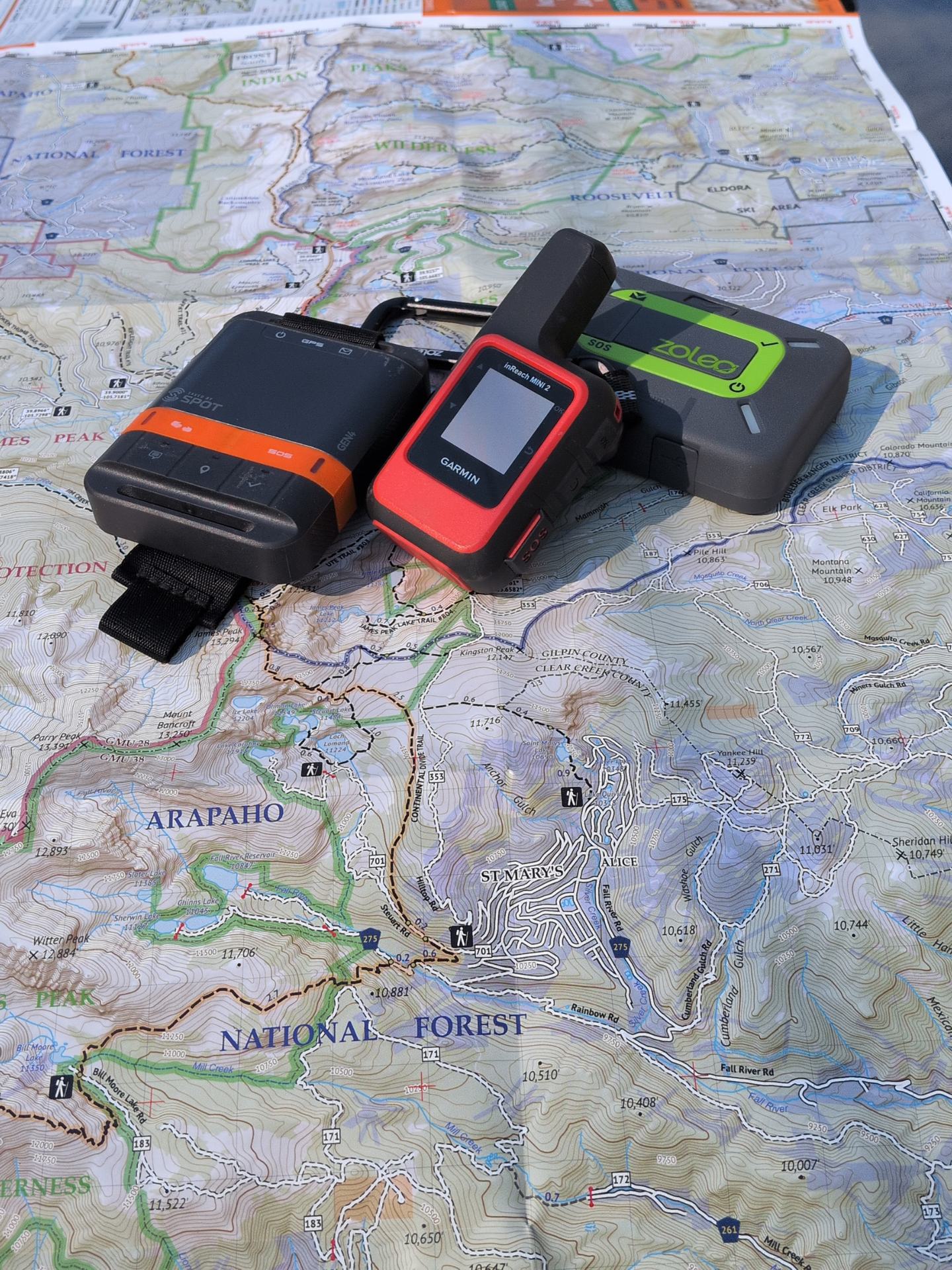 A Garmin inReach Mini 2, a ZOLEO, and a SPOT Gen4 laid out side by side.