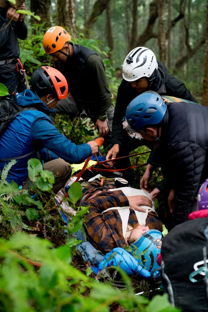 A field scenario in progress on real terrain. People securing a patient into a litter in the backcountry.